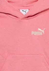 Ροζ φούτερ με κουκούλα, εμπρόσθια τσέπ η και λευκό λογότυπο Puma στο στήθος, που δείχνει την υφή του υφάσματος και τις λεπτομέρειες της κουκούλας.