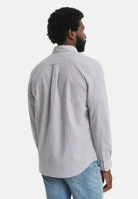 Camicia a maniche lunghe in tessuto leggero a quadri; presenta un colletto a punta, una piega sul retro e polsini con bottone. I colori disponibili includono bianco, blu e rosso.