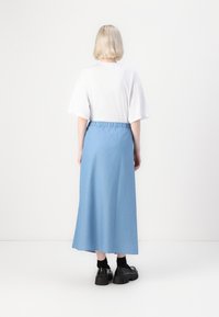 Jupe longue bleu clair en tissu doux avec une taille élastique, associée à un t-shirt blanc ample et des chaussures noires épaisses.