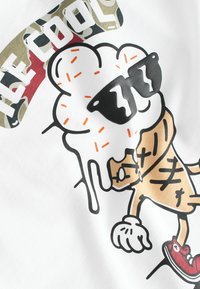 Witte t-shirt met een geïllustreerde ijskegel met een zonnebril, druppelend ontwerp en kleurrijke accenten, waaronder oranje sprinkles en rode schoenen.