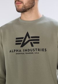 Sudadera verde oliva hecha de una suave mezcla de algodón, con un logotipo impreso en negro, cuello redondo y puños acanalados.