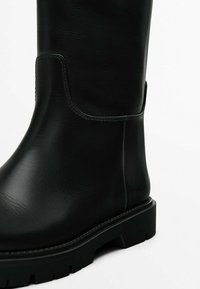 Botte haute noire en cuir avec une finition lisse, semelle en caoutchouc robuste et coutures minimales. Dotée d'un bout rond et d'un talon carré.