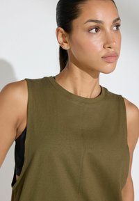 Top senza maniche verde oliva realizzato in tessuto morbido, con scollo rotondo e aperture laterali, progettato per comfort e libertà di movimento.