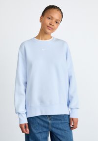 Světle modrá mikina Nike s kulatým výst�řihem, spadlými rameny a žebrovanými manžetami. Na hrudi se nachází malé bílé logo Nike.