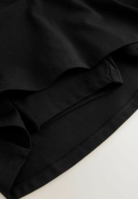 Zwart katoenen stof met een gladde textuur, met overlappende lagen en zichtbare gestikte zomen. Eenvoudig ontwerp zonder patronen of accenten.