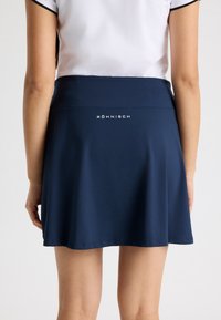 Skort atlético azul marino con una textura suave, que presenta una cinturilla ancha y el nombre de la marca "Röhnisch" impreso en blanco en la parte posterior.