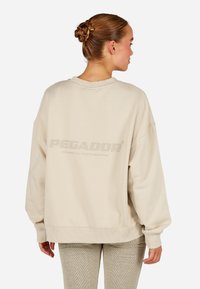 Beige dydžio megztinis su raukšlėmis rankovėse ir apvadu. Ant nugaros yra didelis, toninis "PEGADOR" logotipas. Lygus paviršius.
