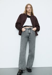 Mustat ja valkoiset kuviolliset leveälahkeiset farkut, joissa on rispaantunut helma, yhdistettynä lyhyeen musta-valkoiseen toppiin ja tumman burgundin väriseen bomber-jakkiin.