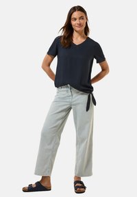 Maglietta corta color navy con scollatura a V e dettaglio con fiocco laterale abbinata a jeans a gamba larga blu chiaro e sandali scuri.