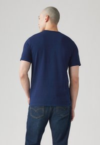 T-shirt bleu marine à manches courtes, col rond, en tissu léger; associé à un jean en denim foncé avec des poches arrière visibles et des coutures.