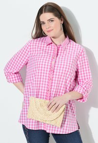 Rosa-weiße Karomuster-Hemdbluse mit aufgerollten Ärmeln, dekorativen Knöpfen und einer seitlichen Schlitzöffnung, kombiniert mit einer gewebten beigefarbenen Clutch.