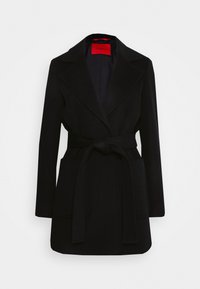 Cappotto nero con cintura, colletto a punta, maniche lunghe e due tasche frontali. Realizzato in un tessuto texturizzato, presenta un'etichetta rossa del marchio all'interno.
