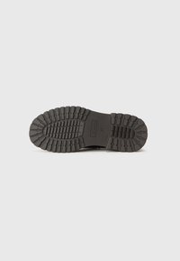 Black rubber shoe sole with deep treads and ridges. Features a smooth, flat area near the center and brand label near the heel.