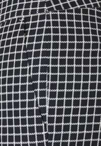 Granatowa tkanina z białym wzorem w kratę z plecionej liny oraz detal pionowej kieszeni z rozcięciem.