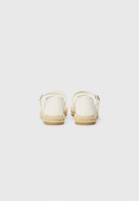 Espadrilles en tissu tissé blanc avec une semelle en corde naturelle et une sangle à la cheville, présentant un motif texturé et sécurisées par une boucle en ton argent.