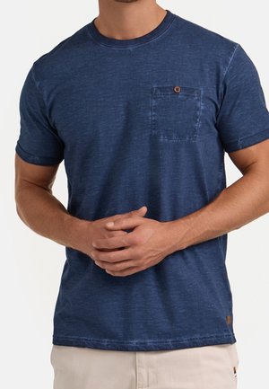 T-shirt en coton bleu marine à manches courtes, col rond, avec une poche poitrine gauche ornée d'un bouton marron. Texture lisse.