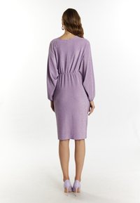 Vestido lila con cintura fruncida, mangas largas y un sutil brillo. Combinado con tacones altos en lavanda a juego.