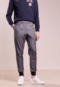 Szare tapered joggery z elastycznym pasem i czarnymi manszetami. Połączone z białymi sneakersami i granatową bluzą z kolorowymi naszywkami.