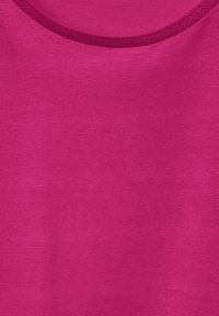Fuchsiové tričko s hladkým povrchem a kulatým výstřihem, který má síťovinový detail kolem límce.