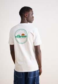 Camiseta blanca de algodón con un logo circular verde y naranja en la parte posterior, de mangas cortas y un corte relajado.
