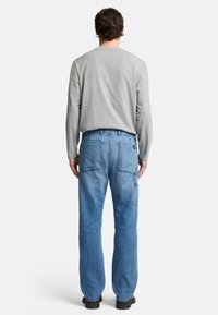 Maglietta grigia a maniche lunghe abbinata a jeans in denim azzurro chiaro, con due tasche posteriori con cuciture visibili e una vestibilità rilassata.