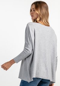 Szary, oversize sweter z długim rękawem, okrągłym dekoltem, ściągaczami na rękawach oraz nieco dłuższym tyłem. Miękka, teksturowana tkanina.