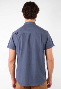 Chemise à manches courtes, bleu foncé, en tissu lisse avec un empiècement au dos, un ourlet arrondi et un petit logo près du col.