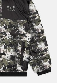 Gepolsterte Jacke mit einem Camouflage-Muster in Schwarz, Grün und Weiß. Verfügt über ein Logo auf der Brust und elastische Bündchen. Glatte, glänzende Textur.