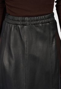 Gonna nera in pelle con vita elastica, texture liscia e design semplice con cuciture verticali per un look sartoriale.