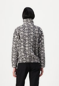 Bluza polarowa z wysokim kołnierzem; biała baza z czarnym wzorem kwiatowym; luźny krój; elastyczny dół i mankiety; teksturowana powierzchnia.