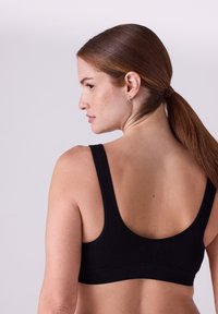 Sort ribstrikket bralette med brede stropper og en glat kant. Har et lavt rygdesign, lavet af blødt materiale, der fremhæver en tætsiddende form.