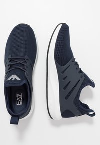 Marineblaue SportSneaker aus Mesh-Gewebe, mit weißen Sohlen, Schnürsenkeln und "EA7 Emporio Armani"-Markierung auf der Zunge und der Innensohle.
