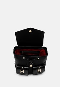 Svart läderryggsäck med gyllene detaljer, texturerad ytfinish, två frampocket och en röd foder inuti med en zip-försluten fack.