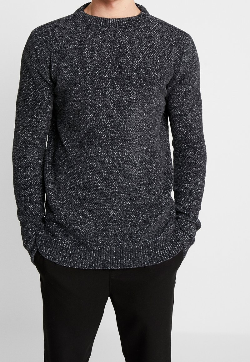 Tmavě šedý pletený svetr s kulatým výstřihem, žebrovanými manžetami a lemem. Tkanina má skvrnitý vzor s bílými akcenty.