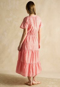 Ružová kvitnúca maxi šaty s krátkymi rukávmi, naťahovacou korpusom a viacvrstvovým volánom na spodnej časti. Ľahký materiál s jemnou textúrou a živou potlačou.