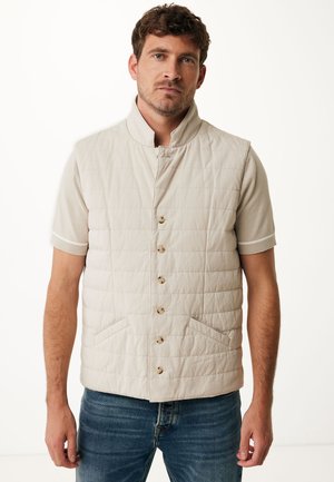 Light beige quilted vest with high collar and button closure, featuring two side pockets and a ribbed short-sleeve shirt underneath.