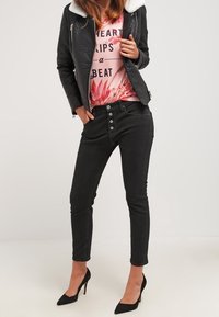 Svart läderbikerjacka med vit pälskrage, rosa grafisk t-shirt med blommönster, svarta skinny jeans och svarta högklackade skor.