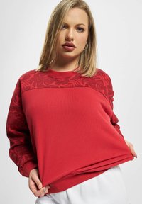 Roter Sweatshirt mit floralem Muster an den Ärmeln und im Schulterbereich, mit Rundhalsausschnitt und lockerer Passform, aus weichem, strukturiertem Stoff.