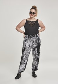 Zwarte top met een kanten paneel, gecombineerd met loszittende zwart-witte broek met een zwirlontwerp. Model draagt zwarte zonnebril en schoenen.