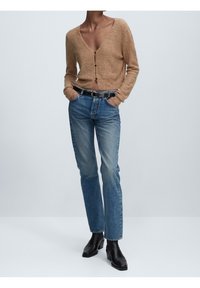 Beiger Strickcardigan mit tiefem V-Ausschnitt, braunen Knöpfen, kombiniert mit hellblauen Jeans mit geradem Bein und schwarzen Stiefeletten.