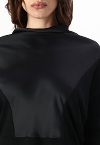 Top nero con una trama liscia simile alla seta sul colletto, abbinato a un tessuto opaco e testurizzato sui lati e sulle maniche.