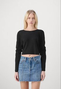 Top crop de manga longa preto com efeito canelado, combinado com uma saia mini de ganga azul clara com bordas desfiadas e bolsos frontais.