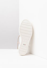 White rubber sole of a shoe with horizontal grooves, featuring a light beige strap attached. "Made in Italy" is embossed on the sole.