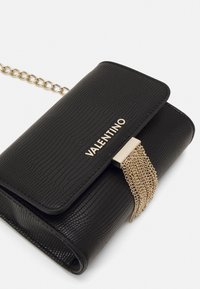 Černá kožená kabelka s texturovaným povrchem, zdobená zlatým řetízkovým přívěskem, magnetickým zapínáním a detaily s logem.