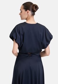 Granatowa sukienka z krótkimi bufkami, gładką satynową fakturą i ozdobnym sznurowanym detalem na tylnej talii.