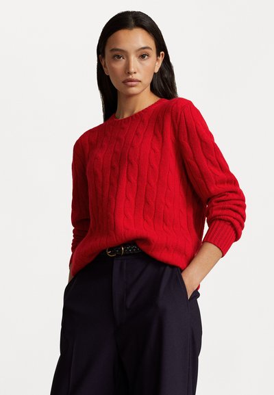 Suéter rojo de punto trenzado con cuello redondo, puños acanalados y corte holgado, combinado con pantalones oscuros, creando un aspecto texturizado en capas.