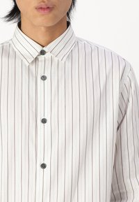 Witte overhem shirt met een verticaal gestreept patroon in lichtbruin. Zachte stof, puntige kraag en grijze knopen aan de voorkant.