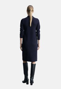 Abito di maglia navy con maniche lunghe, lunghezza al ginocchio, con un colletto alto. Abbinato a stivali neri con tacco alto, al ginocchio.