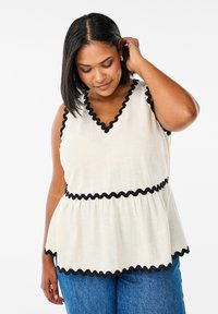 Bílý peplum top s černým vlnkovým lemováním podél výstřihu a pasu, vyFeaturing hladký povrch a výstřih ve tvaru V.