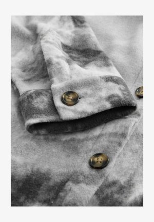 Gray fleece fabric with a mottled pattern, featuring a button closure and folded cuff detail. Soft texture and muted color palette.